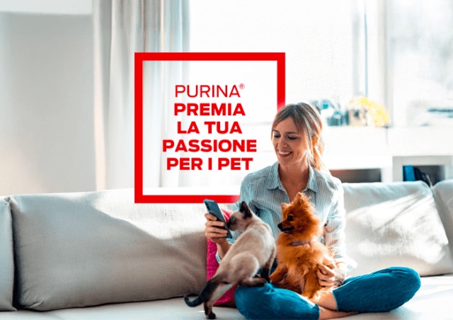 ragazza seduta su un divano bianco con un cane e un gatto in braccio, con in mano uno smartphone. Alla sua sinistra, il testo:'Purina premia la tua passione per i pet'