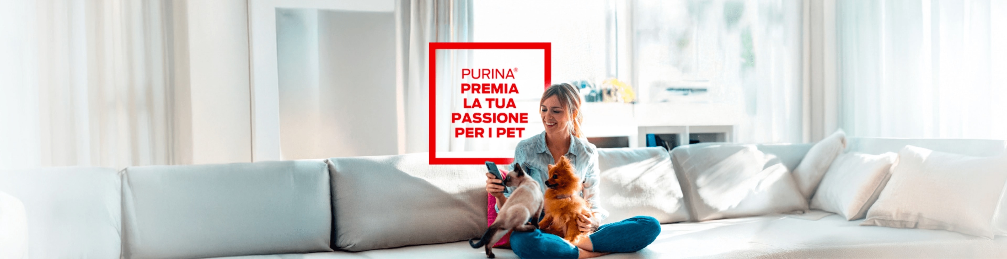 ragazza seduta su un divano bianco con un cane e un gatto in braccio, con in mano uno smartphone. Alla sua sinistra, il testo:'Purina premia la tua passione per i pet'