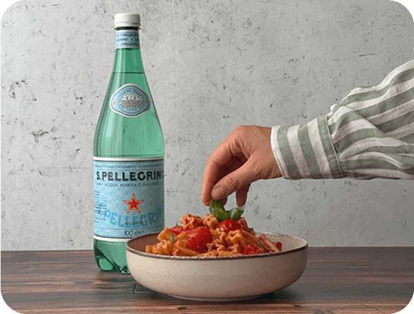 Una pianta di basilico, pasta Garofalo e una bottiglia San Pellegrino. In basso su una banda rossa il testo:'Vinci e porta in tavola le stelle'