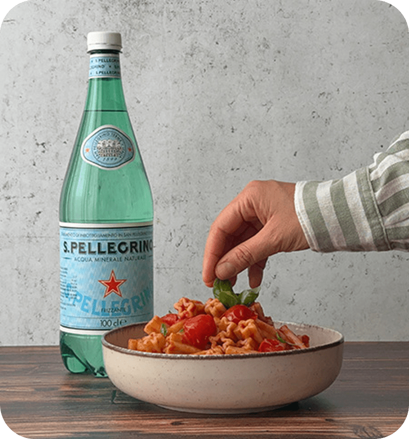 Una pianta di basilico, pasta Garofalo e una bottiglia San Pellegrino. In basso su una banda rossa il testo:'Vinci e porta in tavola le stelle'